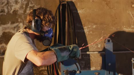 caucasian male blacksmith wearing breathing mask forging metal tool in workshop