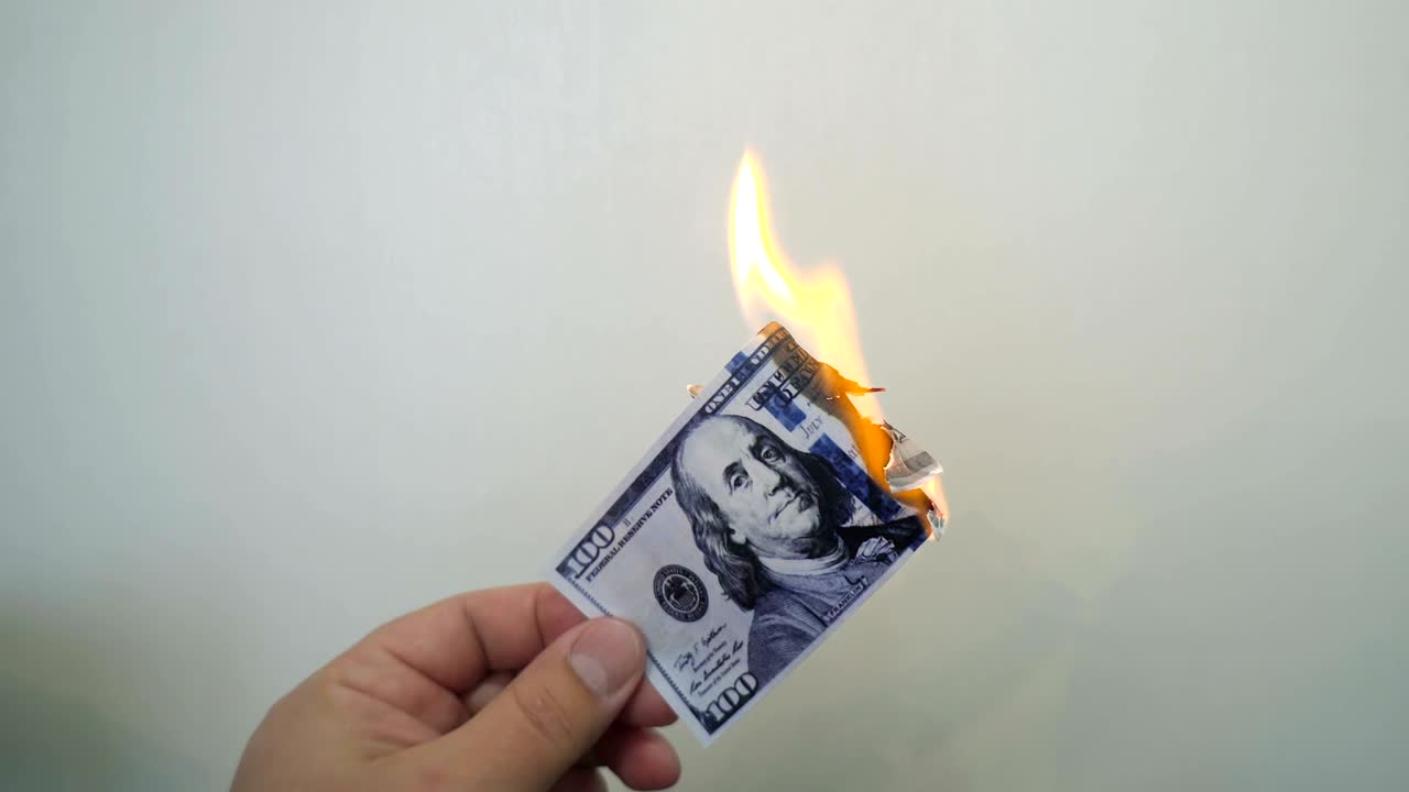 Hand holding a burning hundred dollar banknote