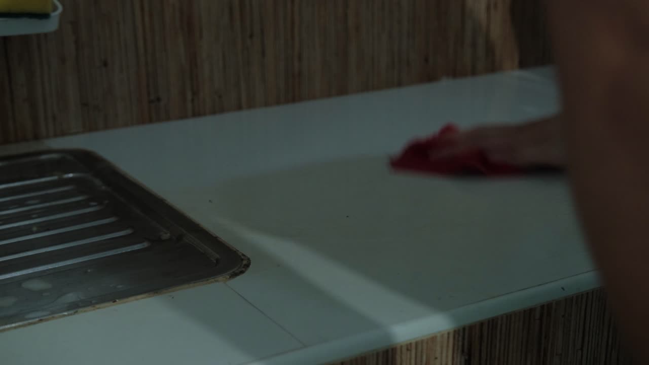Close-up shot of young man wiping down and cleaning kitchen counter with rag.