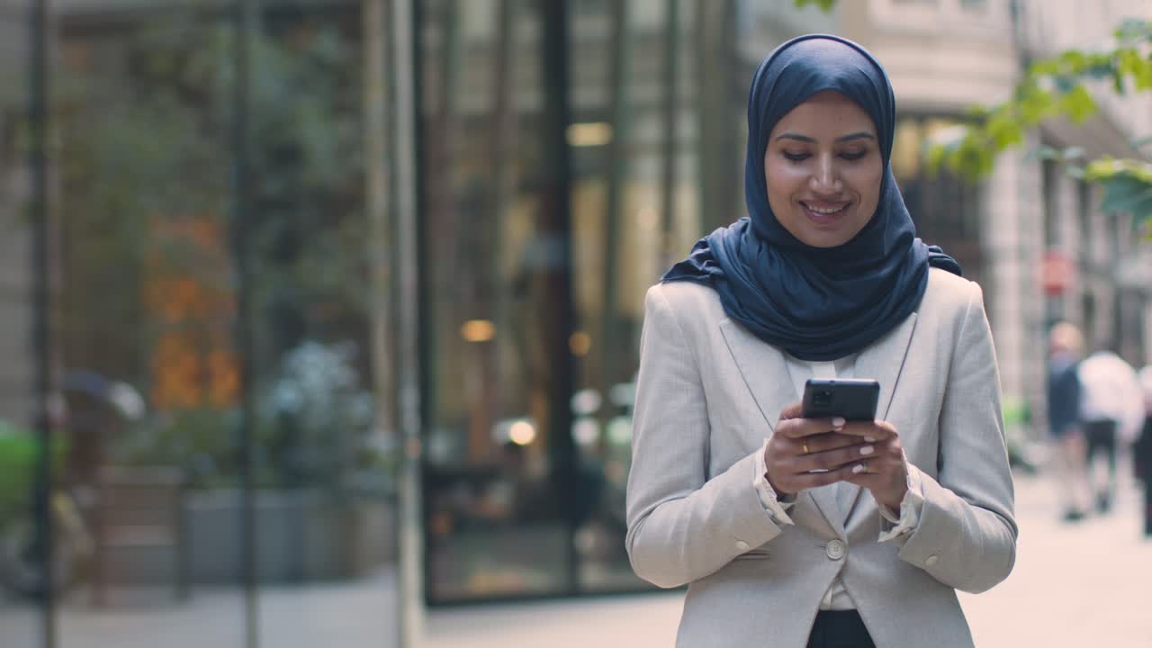 Muslim Businesswoman Checking Messages On Mobile Phone Standing Outside Office In City 3