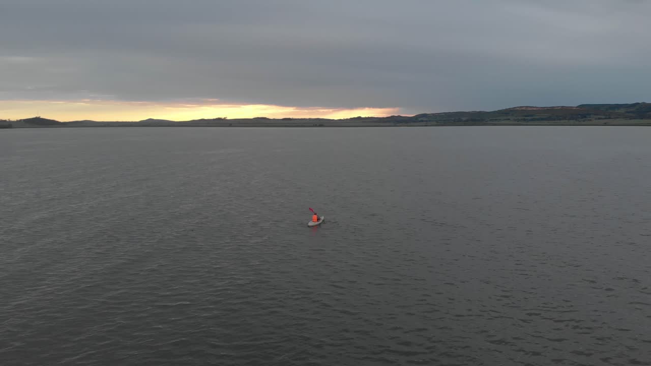 órbita aérea alrededor con un chaleco salvavidas naranja en kayak en el lago victoria con el sol saliendo en el horizonte