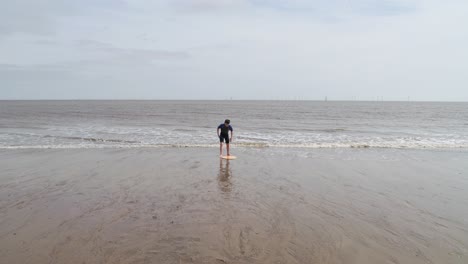 young boy in a wetsuit on a beach digging in the sand