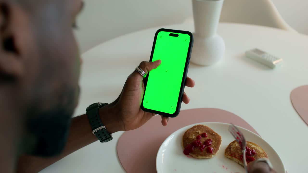 persona comiendo el desayuno mientras usa un teléfono de pantalla verde