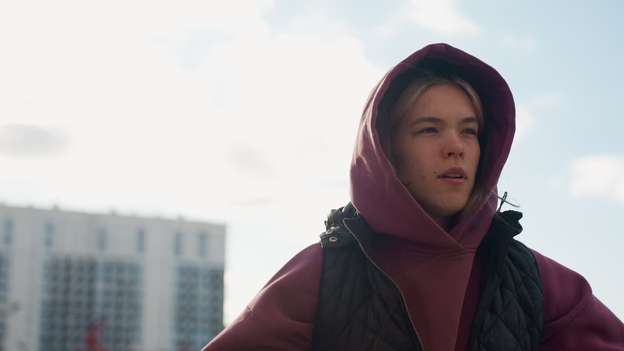 Trainer in hoodie and vest jumps energetically during warm up routine under bright sun on urban pavement surrounded by residential buildings and autumn foliage, showcasing dynamic strength movement