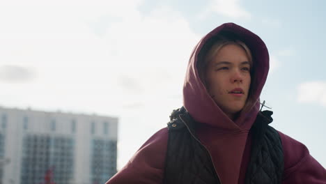 trainer in hoodie and vest jumps energetically during warm up routine under bright sun on urban pavement surrounded by residential buildings and autumn foliage, showcasing dynamic strength movement