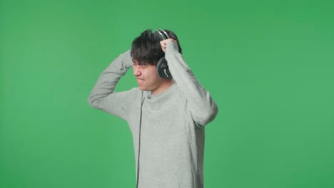 side view asian man listening to music with headphones and dancing in the green screen studio