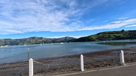 a serene drive along akaroa's waterfront captures stunning landscapes, calm waters, and clear skies in vibrant daylight