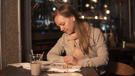 woman painting a t-shirt in a cafe at night