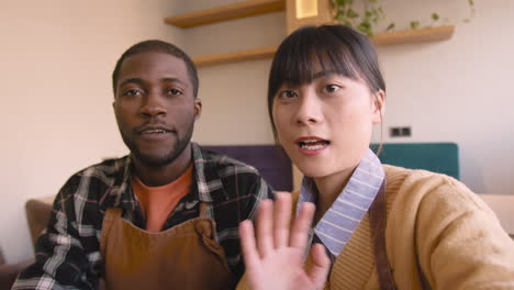 waiter and waitress taking a selfie video and talking to camera while sitting at table in coffee shop