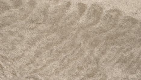 Sand-particles-move-because-of-water-stream,-close-up