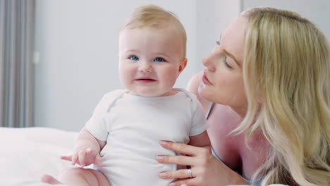 mother lying on bed at home gives baby son kiss