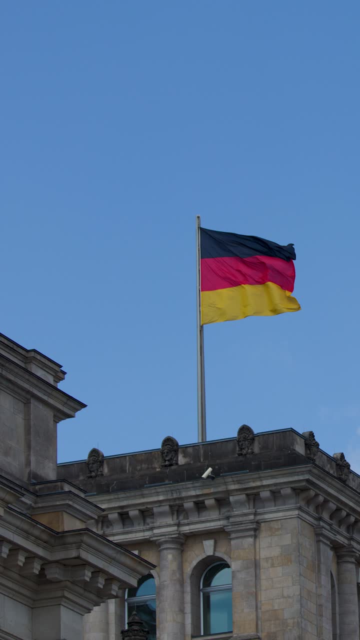 Bendera Jerman berkibar di atas bangunan batu bersejarah di bawah langit cerah, kamera statis, cahaya alami