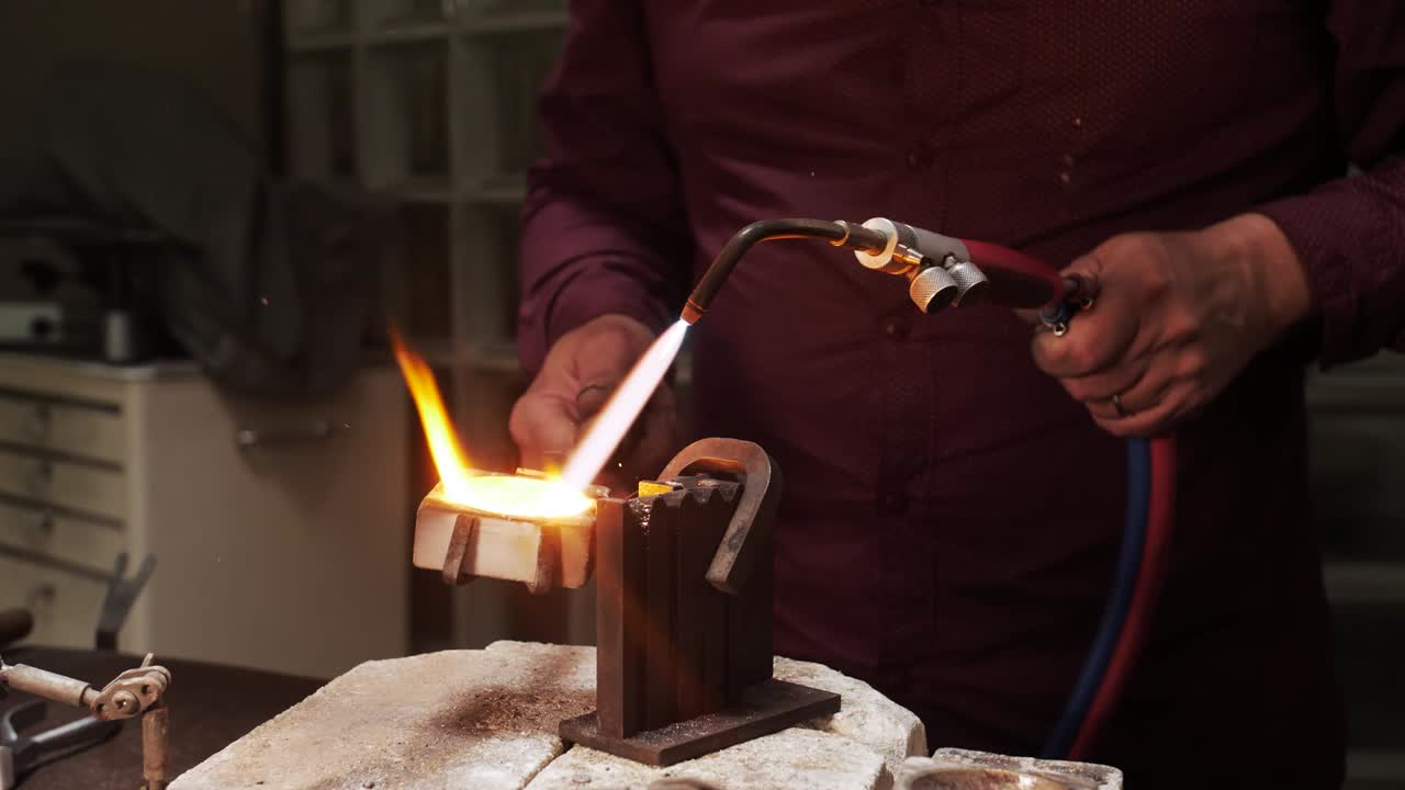 verter oro fundido en un molde de metal mientras se calienta con un soplete de gas