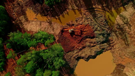 topdown orbit view of heavy machinery during deforestation, treetops and muddy ponds at development site