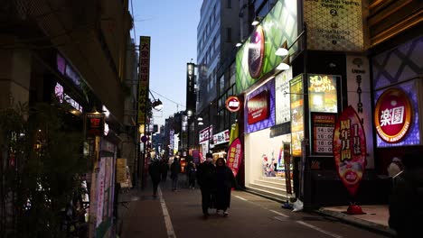 pedestrians walking under illuminated billboards at dusk.