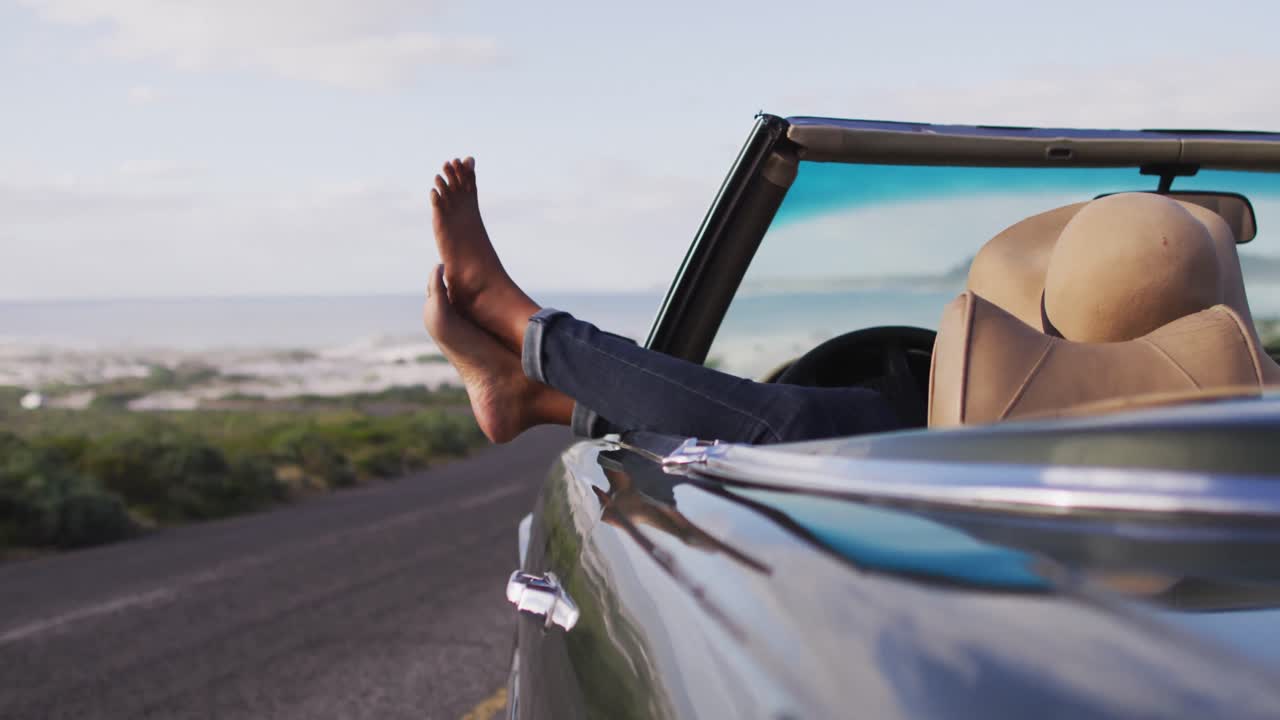 mujer afroamericana sentada con los pies en la ventana de un coche convertible
