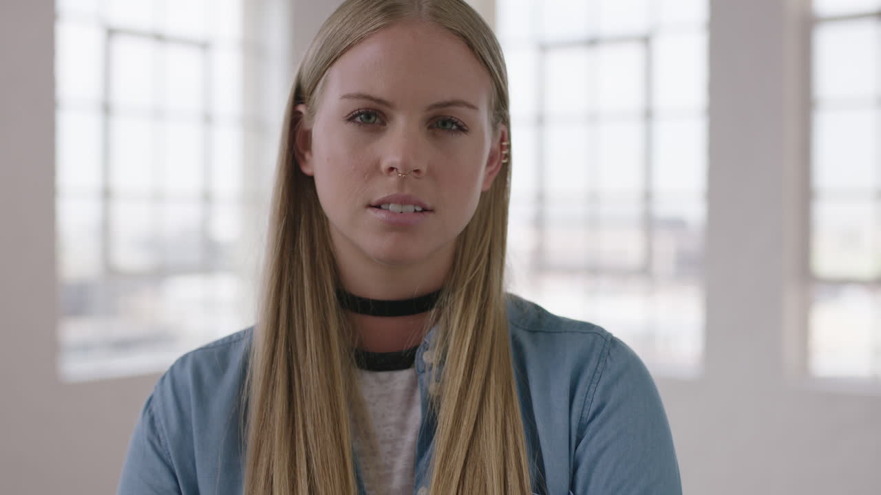 retrato en primer plano de una hermosa mujer rubia joven que parece seria y pensativa ante la cámara vistiendo una moda relajada y elegante en el fondo de las ventanas del apartamento