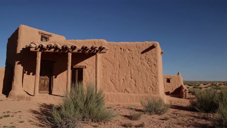 adobe dwelling nestled in arid terrain, blending rustic southwestern architectural style with sandy landscape under bright azure sky, emphasizing natural earth toned textures