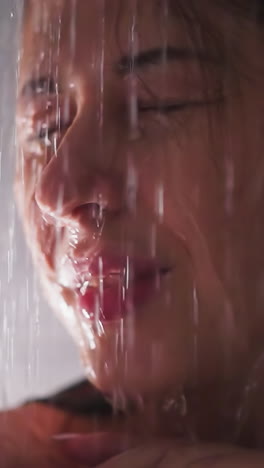 positive woman with water drops on face in shower unit closeup. pretty lady enjoys warm jets washing body in home bathroom. relaxation in washroom