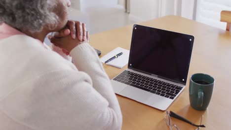 Portrait-of-senior-african-american-woman-sitting-at-table,-using-laptop-with-copy-space