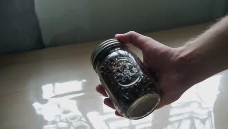 static shot of hand holding mason jar full of single-origin coffee beans.