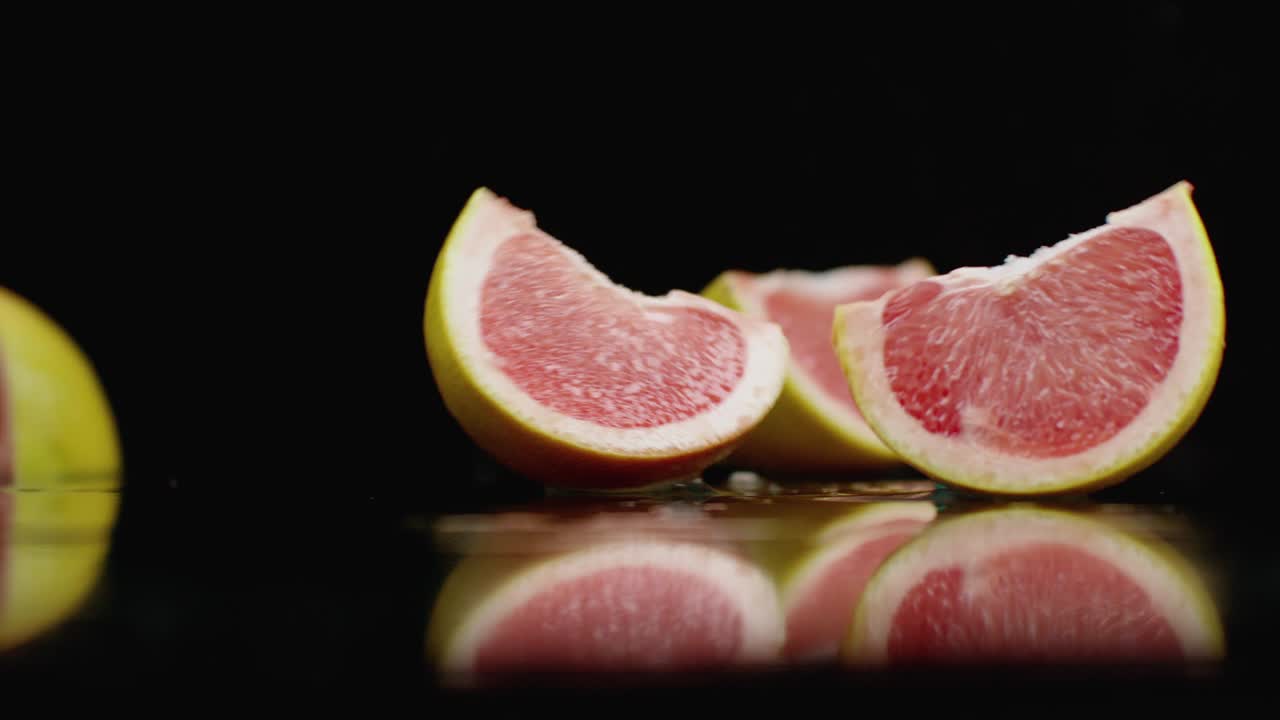 pomelo picante rojo en rebanadas cayendo sobre un vaso con salpicaduras de agua en cámara lenta sobre un fondo oscuro.
