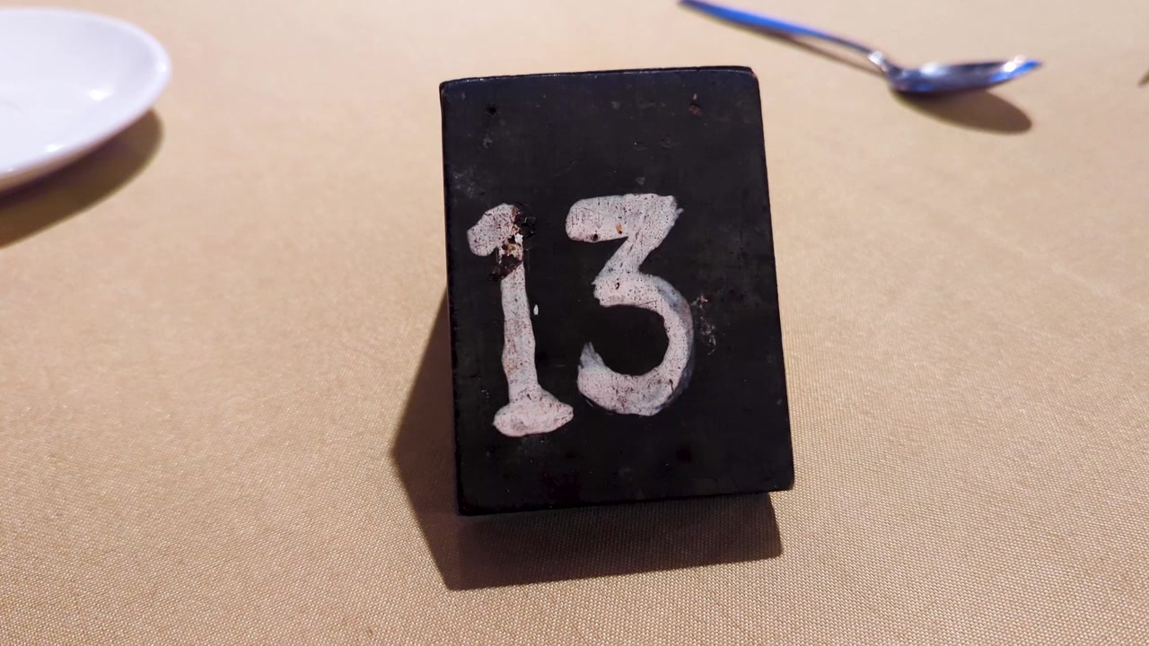 Handgezeichnete Tischnummer 13 (dreizehn) in weißer Kreide auf einer Tafel, platziert auf einem Restauranttisch