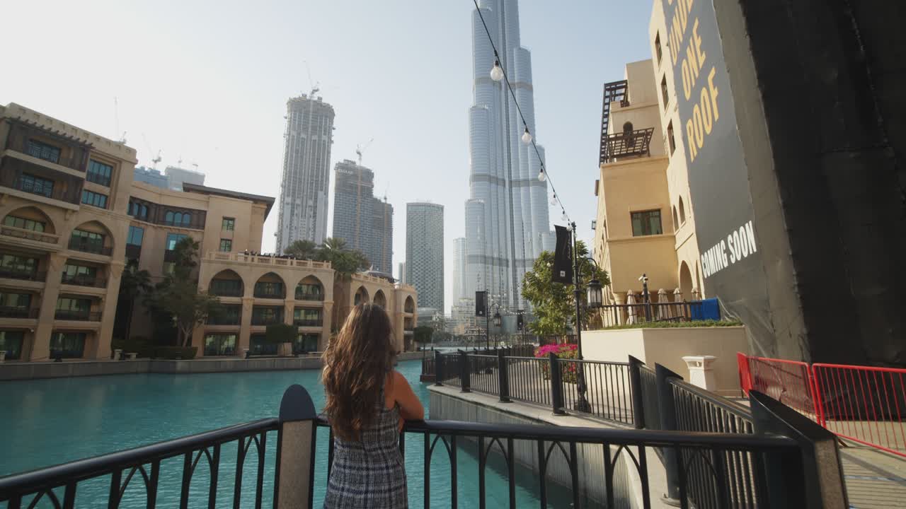 Woman watching Burj Khalifa skyscraper by the pool in Dubai. Tourist exploring metropolitan city center of Dubai