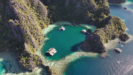 aerial drone view of coron island’s dramatic cliffs, tropical greenery, and idyllic turquoise waters. downward rotating shot of bugalows in the lagoon.