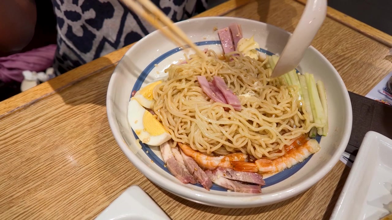 Inquadratura dall'alto di una persona che mescola noodles ramen con gamberetti e prosciutto usando le bacchette