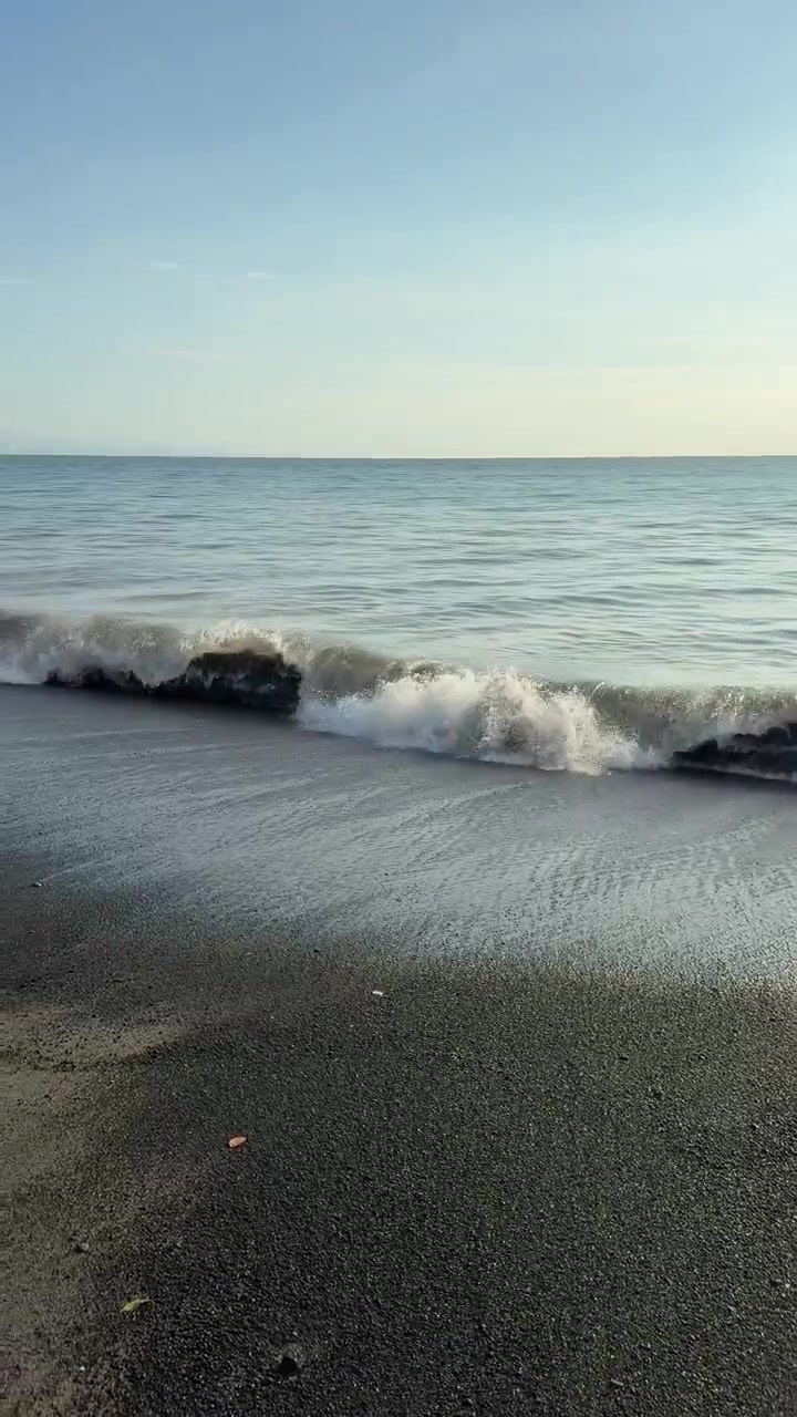 Dolci onde oceaniche che si infrangono su una spiaggia scura.