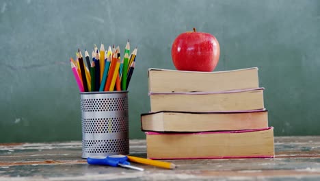 apple on book stack with school supplies on table