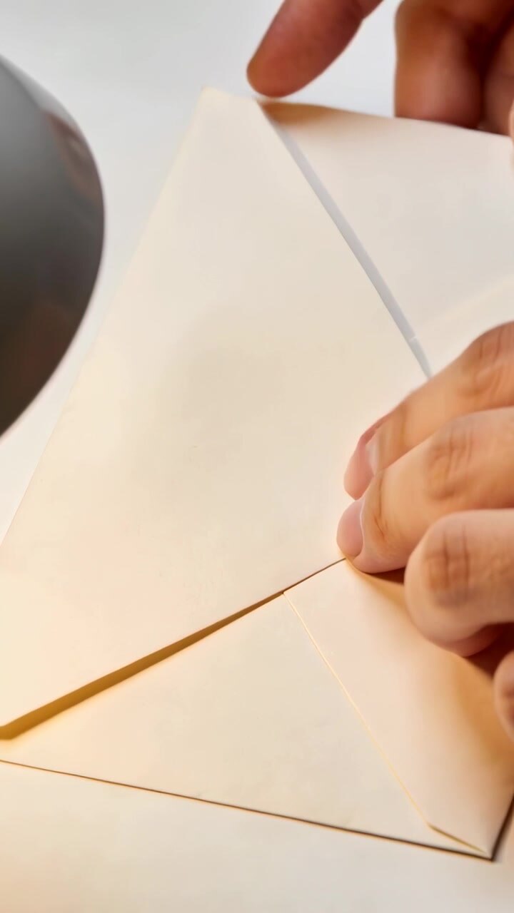 Video verticale: Mano che si estende a destra sigillando una busta posizionando e premendo un sigillo rosso su una scrivania, con una lampada