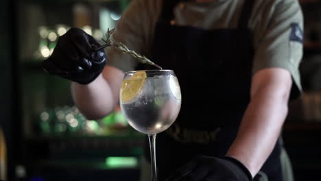 bartender-garnishes-cocktail-with-rosemary-in-glass