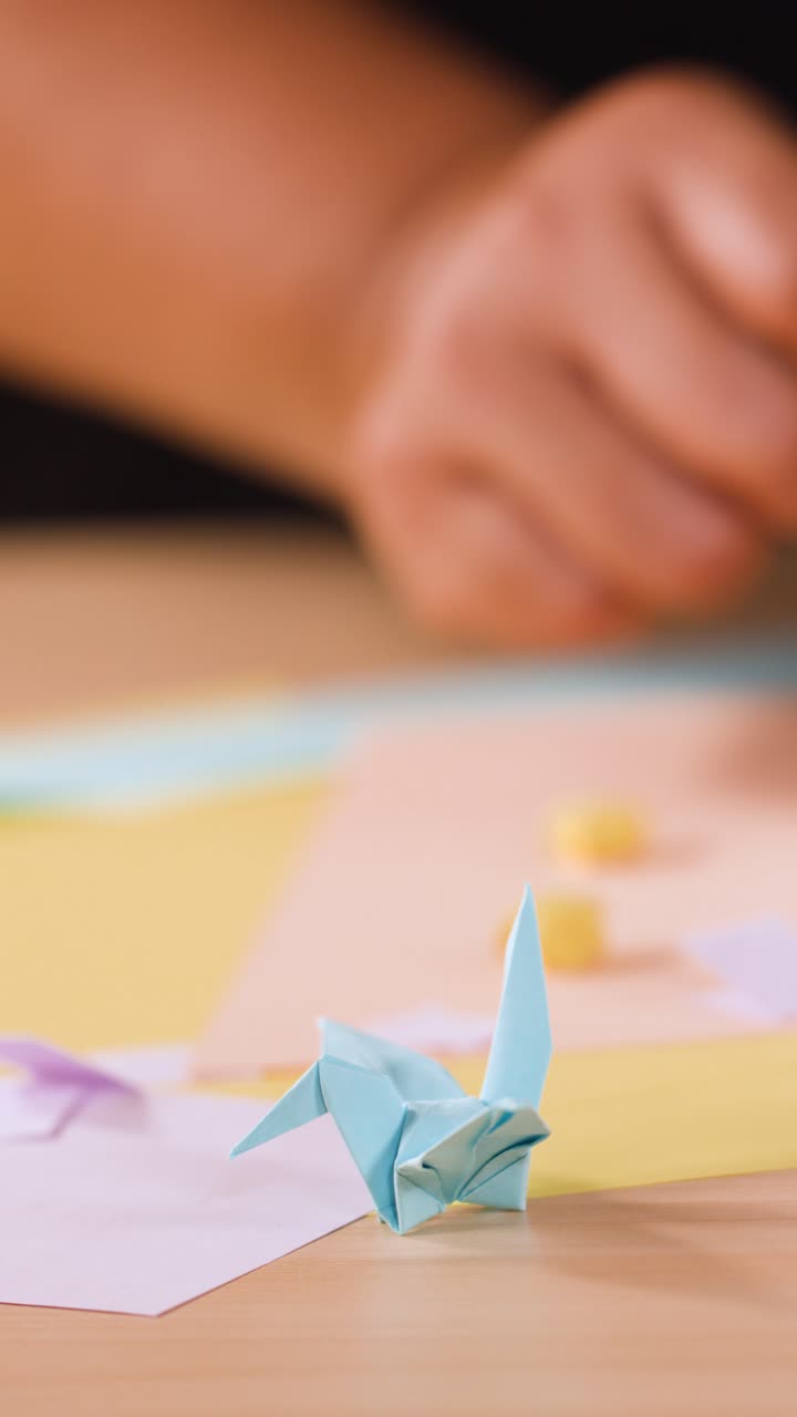 A person folds paper into origami shapes with a blue crane in the foreground