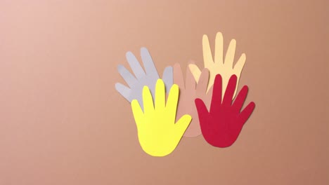 Close-up-of-hands-together-made-of-colourful-paper-on-brown-background-with-copy-space