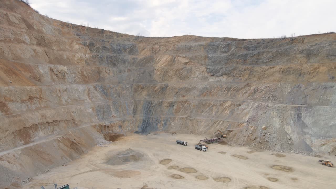 Drone shot rising in front a large quarry site with machines at work, cloudy day
