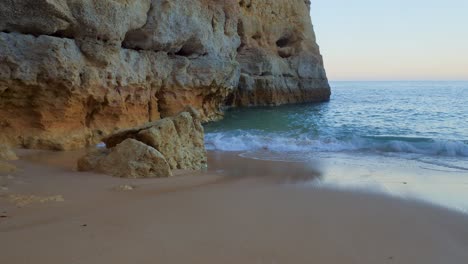Ground-level-footage-of-waves-lapping-on-a-tiny-idyllic-deserted-sandy-cove-in-Algarve,-Portugal