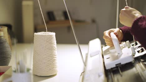 manos femeninas usando la máquina de tejer para tejer tela en el taller