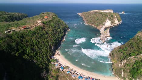 sand atuh beach and lagoon with rolling foamy waves in nusa penida, bali, indonesia - aerial pull back