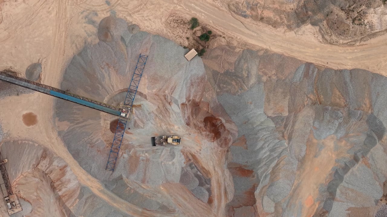 An aerial view captures a vast industrial quarry with heavy machinery and conveyor belts actively processing raw construction aggregates.