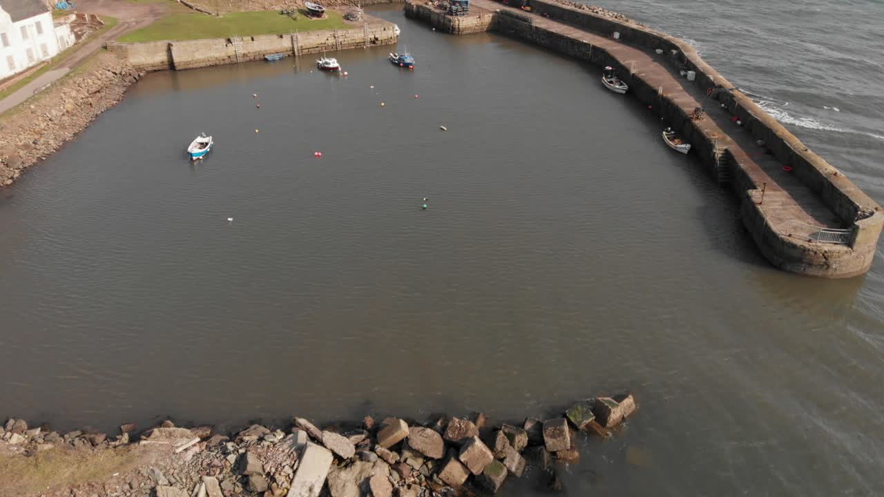 Sorvolo aereo del piccolo porto storico a West Wemyss Fife, Scozia, con piccole barche da pesca, onde dolci e luce solare.