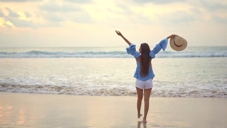 a young healthy woman slowly walks along the wet sand into the incoming ocean waves