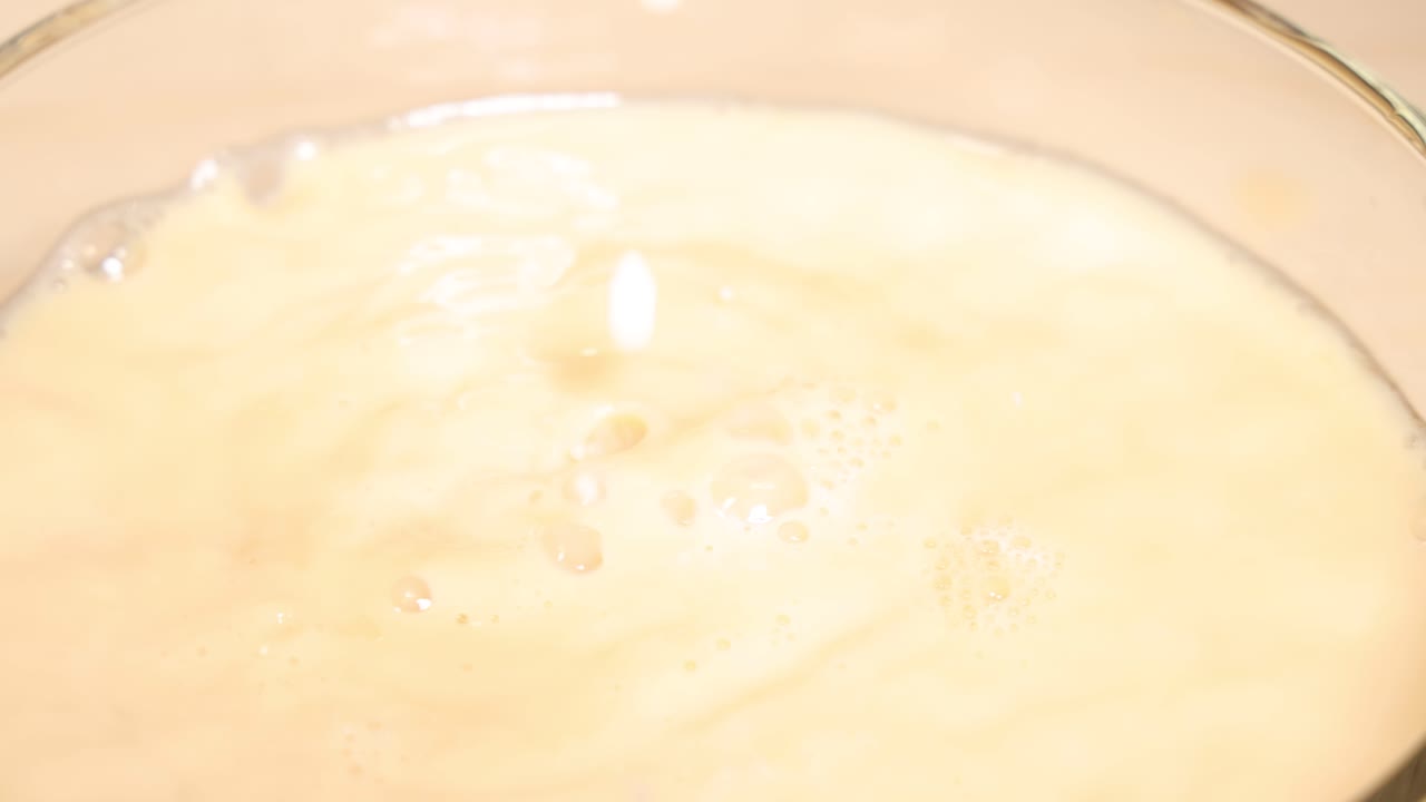 Milk blends into tea, creating swirling patterns in a glass cup against a dark backdrop