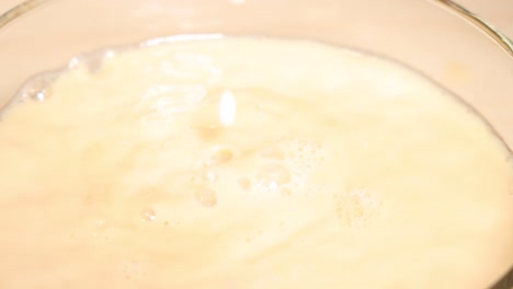 milk blends into tea, creating swirling patterns in a glass cup against a dark backdrop