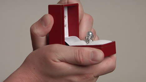 a man's hands open a red jewelry box that reveals a pearl ring