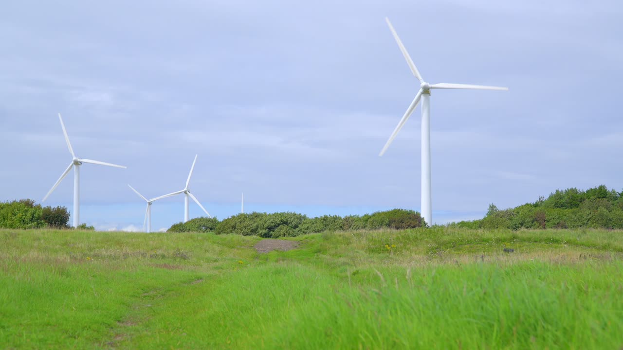 구름이 많은 여름 날 에 회전 하는 풍력 터빈 을 향해 잔디 잔디 를 가로지르고 있다