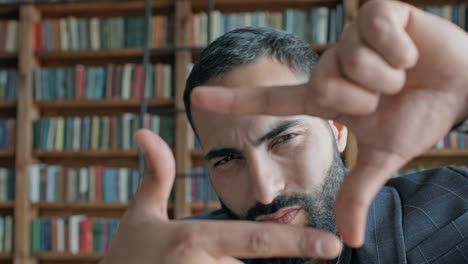 young man from the middle east in the library makes square with his hands like frame and looks at it.