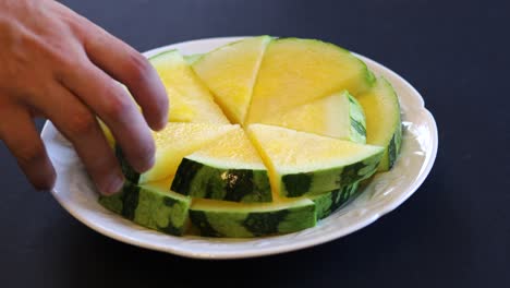 Die-Hand-Eines-Mannes-Nimmt-Ein-Stück-Gelbe-Wassermelone-Von-Einem-Teller