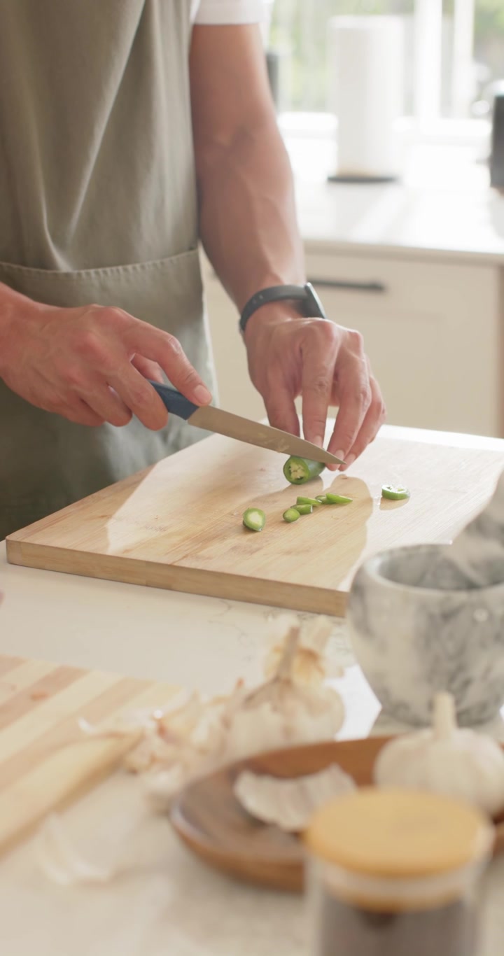 Video verticale: Coltello che taglia zucchine sul bancone con un pezzo tenuto in mano e mani che sbucciano aglio per un pasto